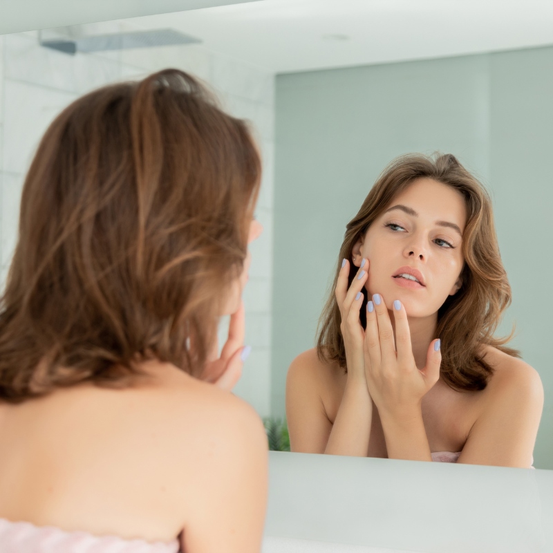 woman looking at their skin in the mirror-